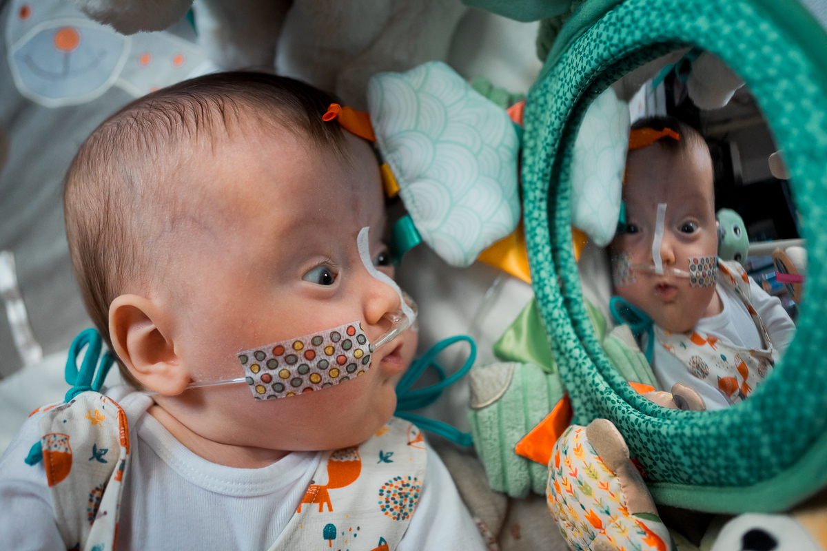 A baby lying on a play mat watching itself in a mirror.