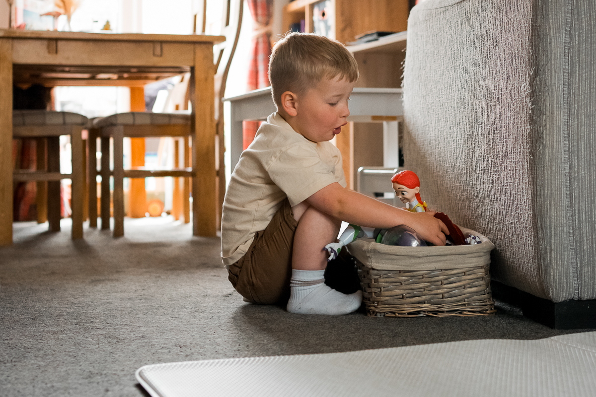 A young boy picking a toy from a box on the floor in the home.