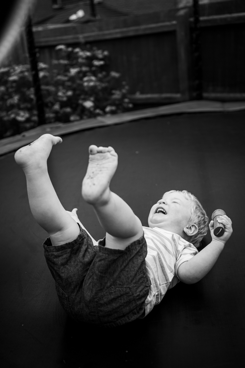 A toddler lying on his back laughing on a trampoline with his feet up high.