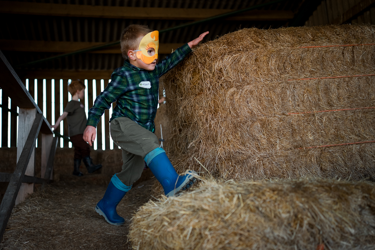 A young boy wearing a colourful mask running around hay bales.