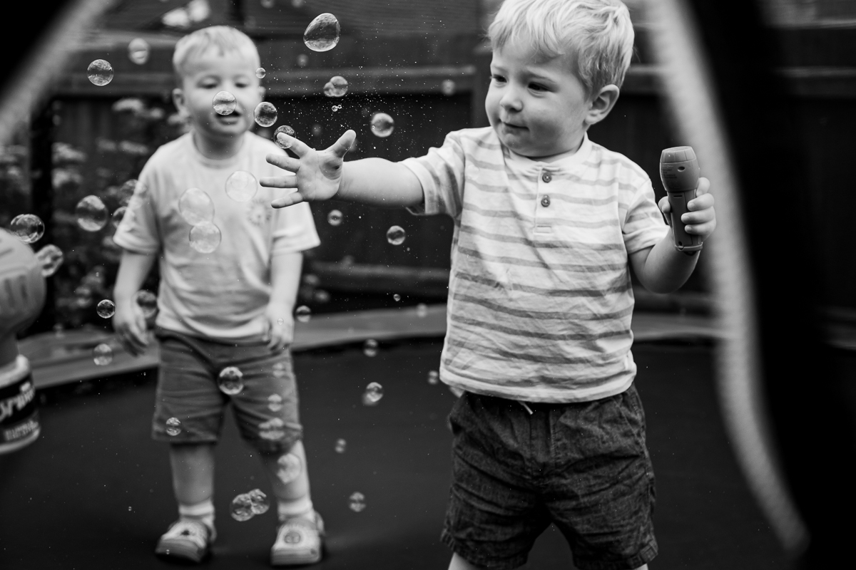 Two toddlers playing with soap bubbles on a trampoline.