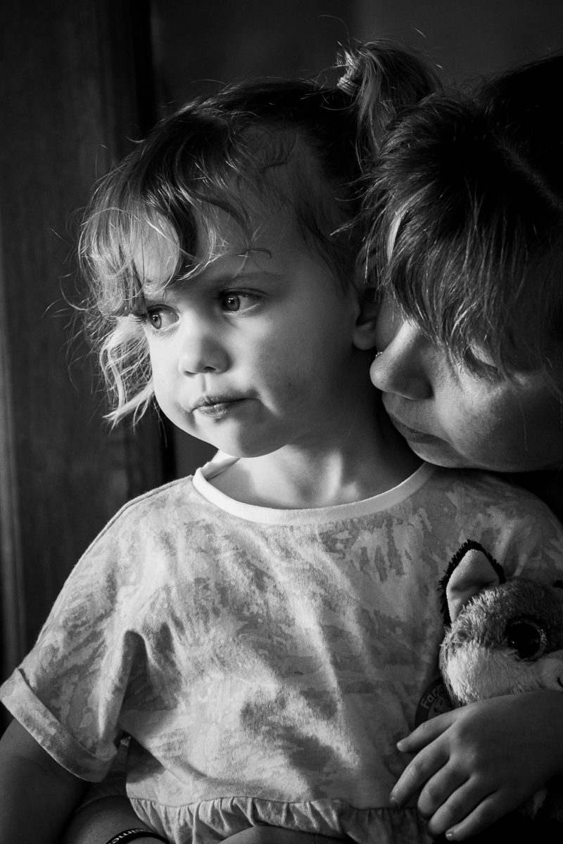 Natural portrait of a young girl being gently embraced by her mother leaning in closely. 