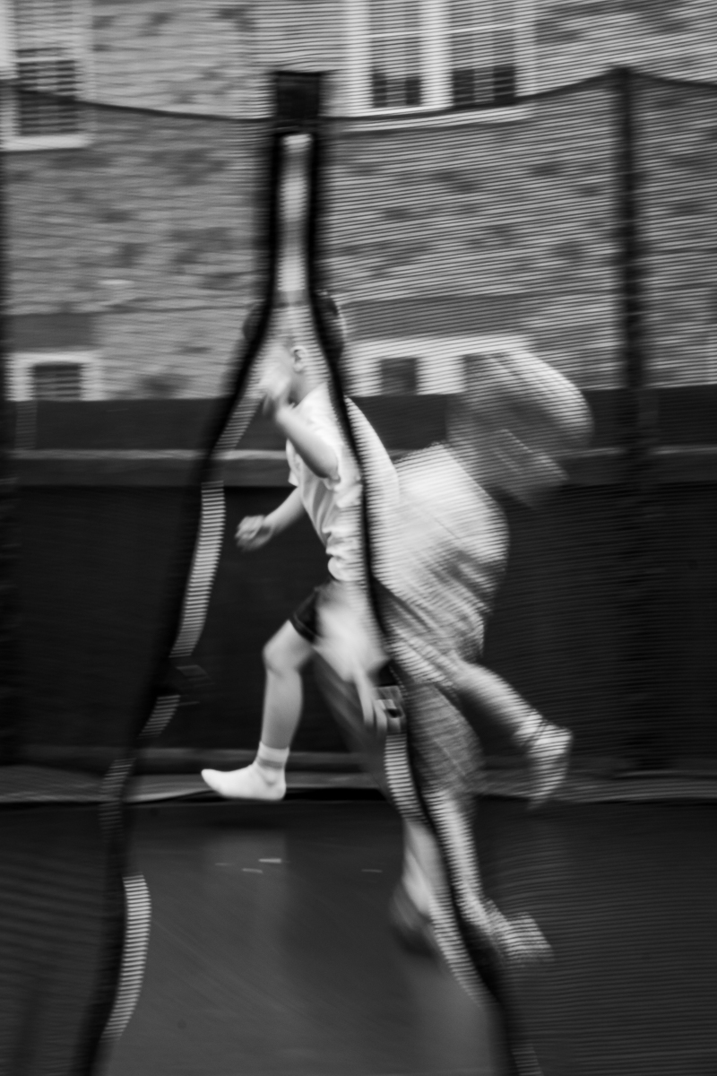Two young boys playing energetically on a trampoline in a backyard.