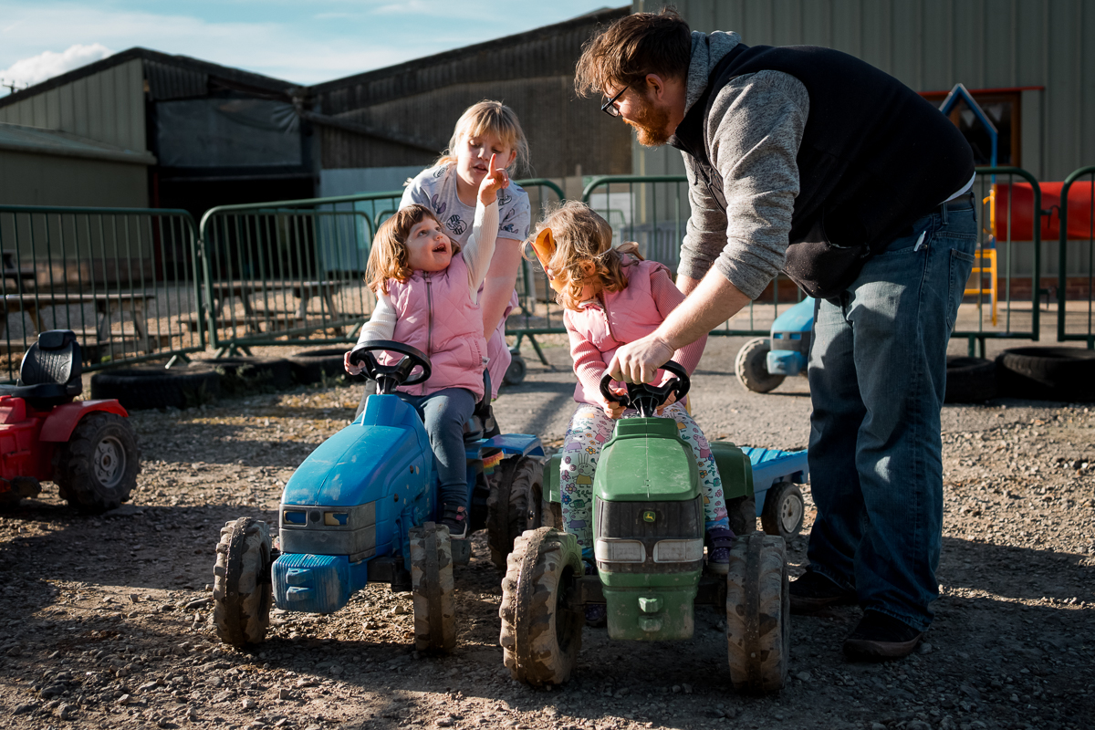 Two young girls riding tractors, one pointing with her finger towards the sky.
