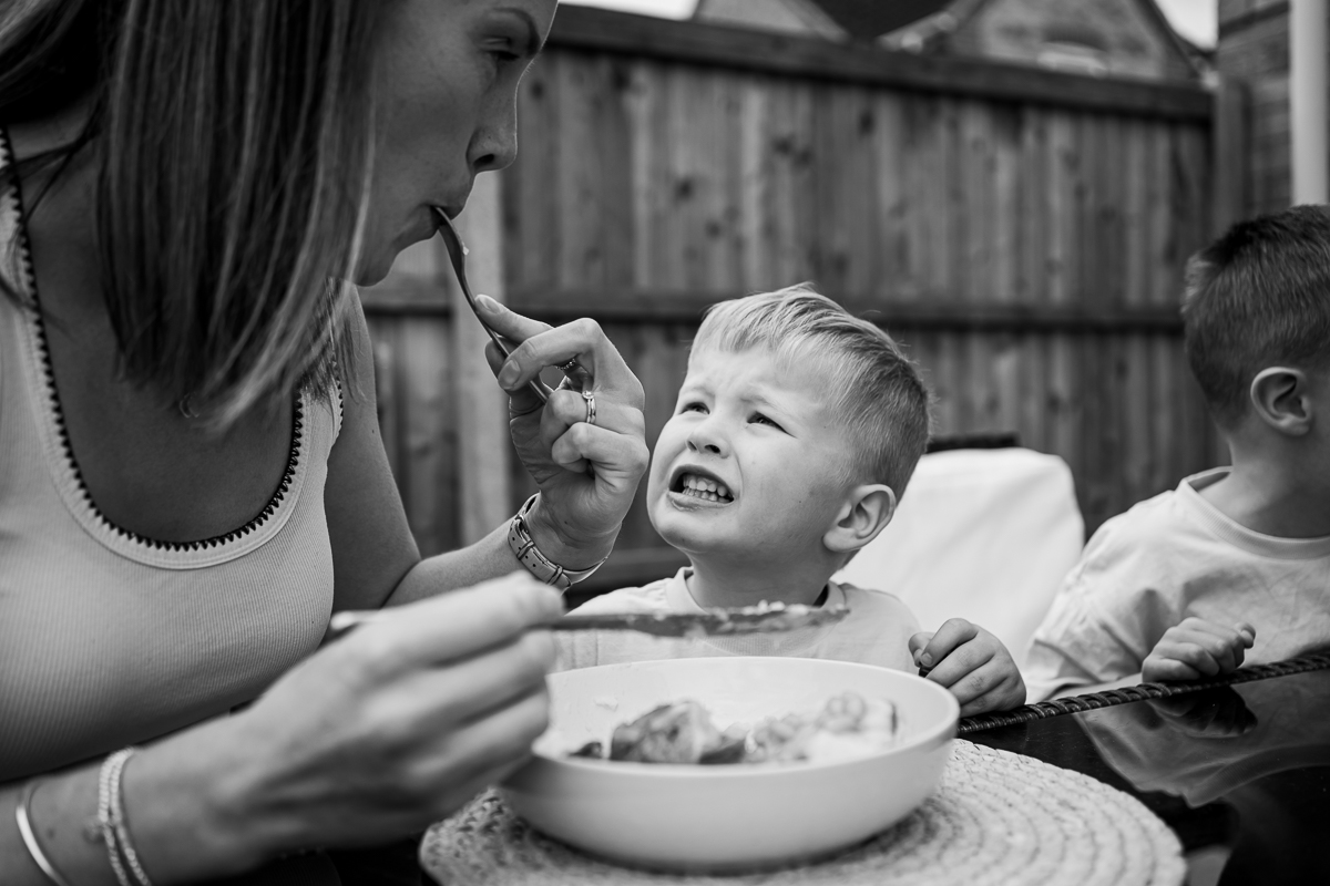 A young boy impatiently staring at his mother eating her meal.
