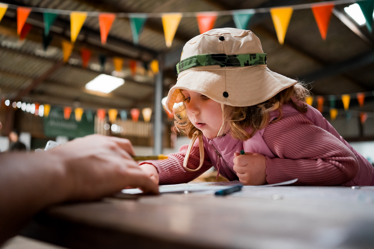 A young girl with a hat drawing a picture at a table in a party room.