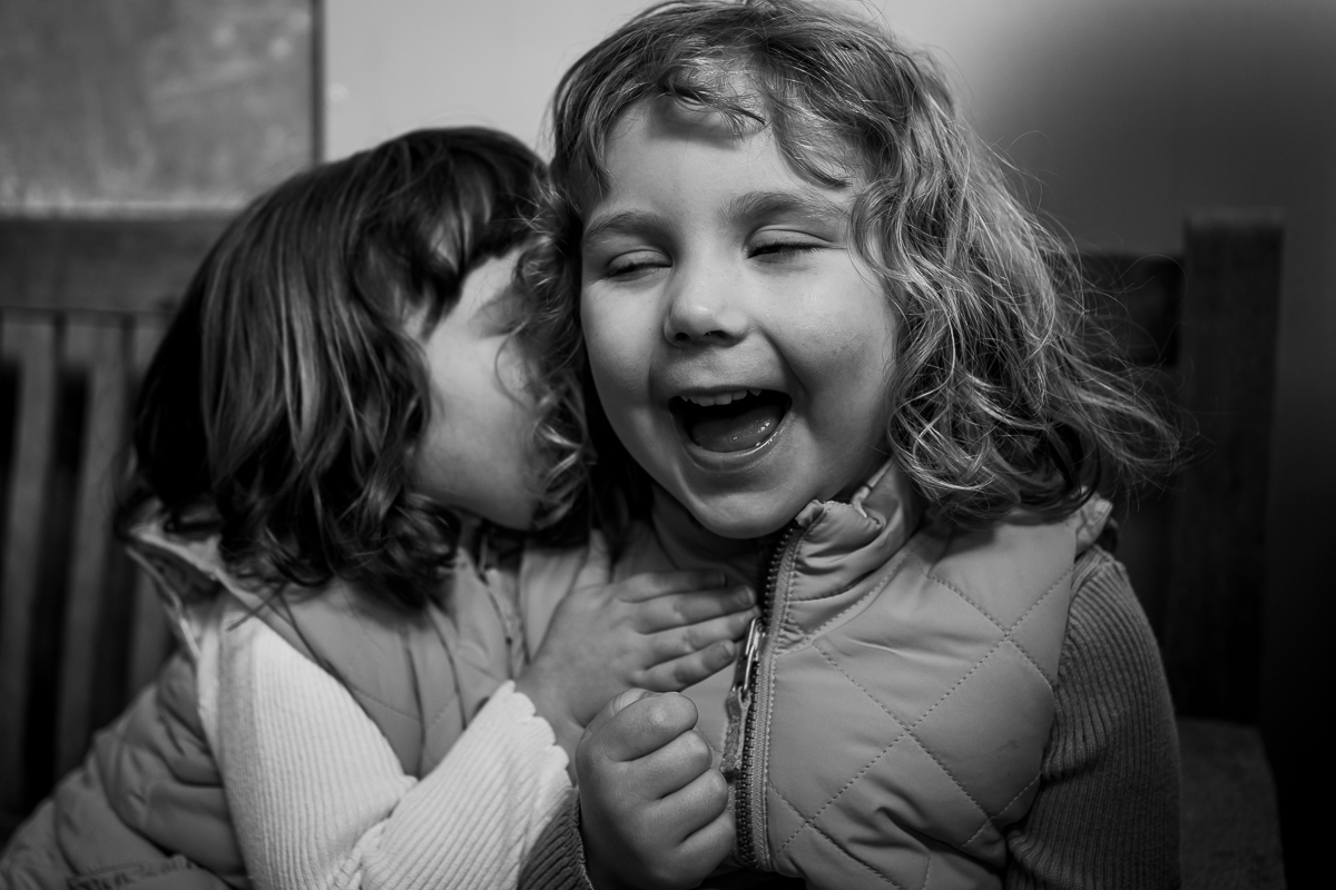 One young girl whispering into another girl’s ear and making her laugh.
